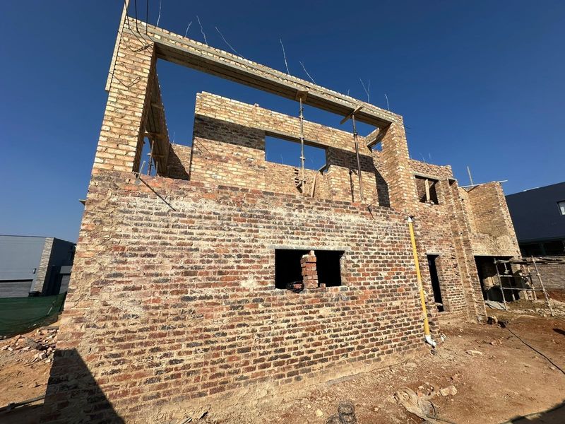 A rear view of a residential property currently under construction, featuring exposed brickwork and structural concrete lintels.