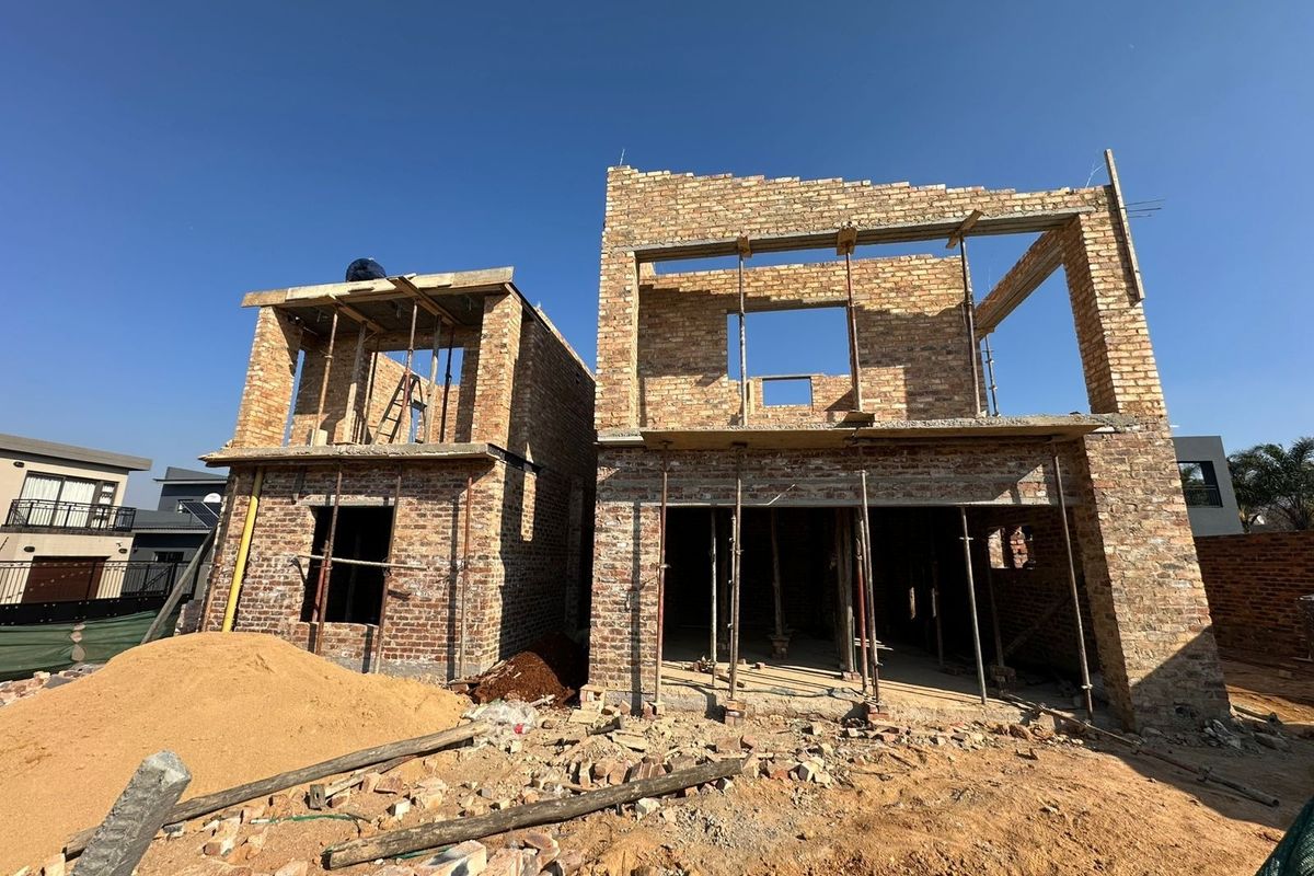 A rear view of a double-story residential property currently under construction, featuring exposed brickwork and structural support props.