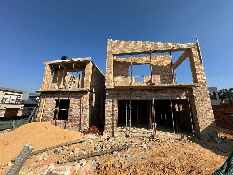 A rear view of a double-story residential property currently under construction, featuring exposed brickwork and structural support props.