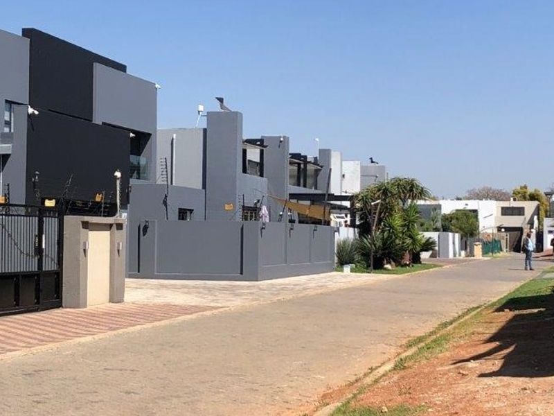 A street-level view of a modern residential complex featuring contemporary grey facades, paved driveways, and secure perimeter fencing.