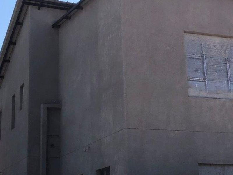 Exterior view of a house under construction featuring unfinished plastered walls and window openings awaiting glazing.
