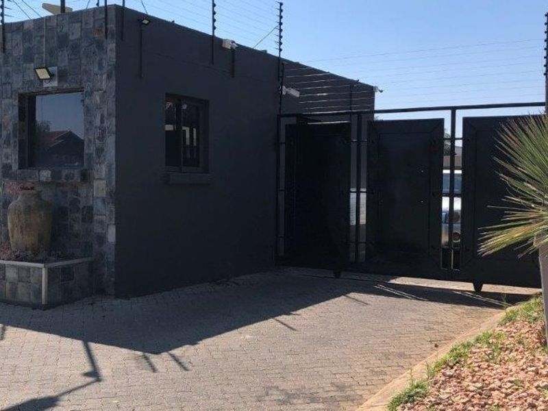 Secure gated entrance featuring a stone-clad guard house, automated metal security gate, and perimeter electric fencing.