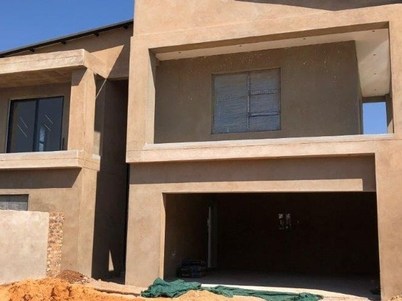 A double-storey residential property under construction, featuring a plastered facade, integrated garage, and balcony, currently in the finishing stages of development.