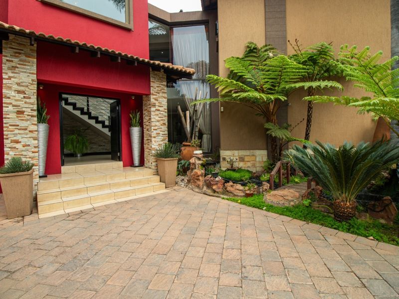 The front entrance features a striking red facade with stone accents, tiled steps, and a beautifully landscaped garden with a water feature.