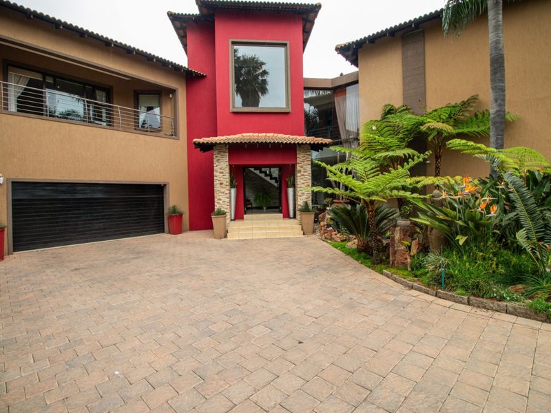 A striking front elevation featuring a bold red entrance tower, stone accents, a paved driveway, and a double garage with a well-maintained garden.