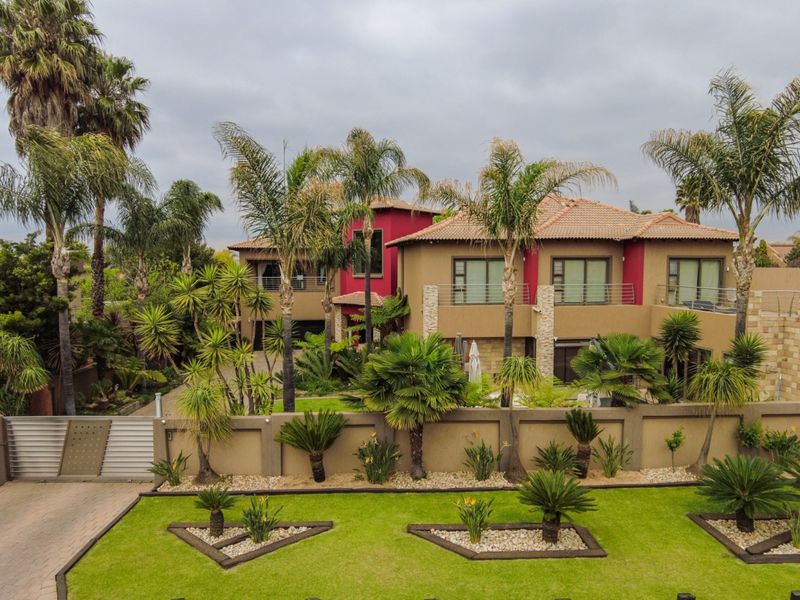 An elevated view of a multi-story residential property featuring a landscaped front garden, paved driveway, stone accents, and a secure boundary wall.