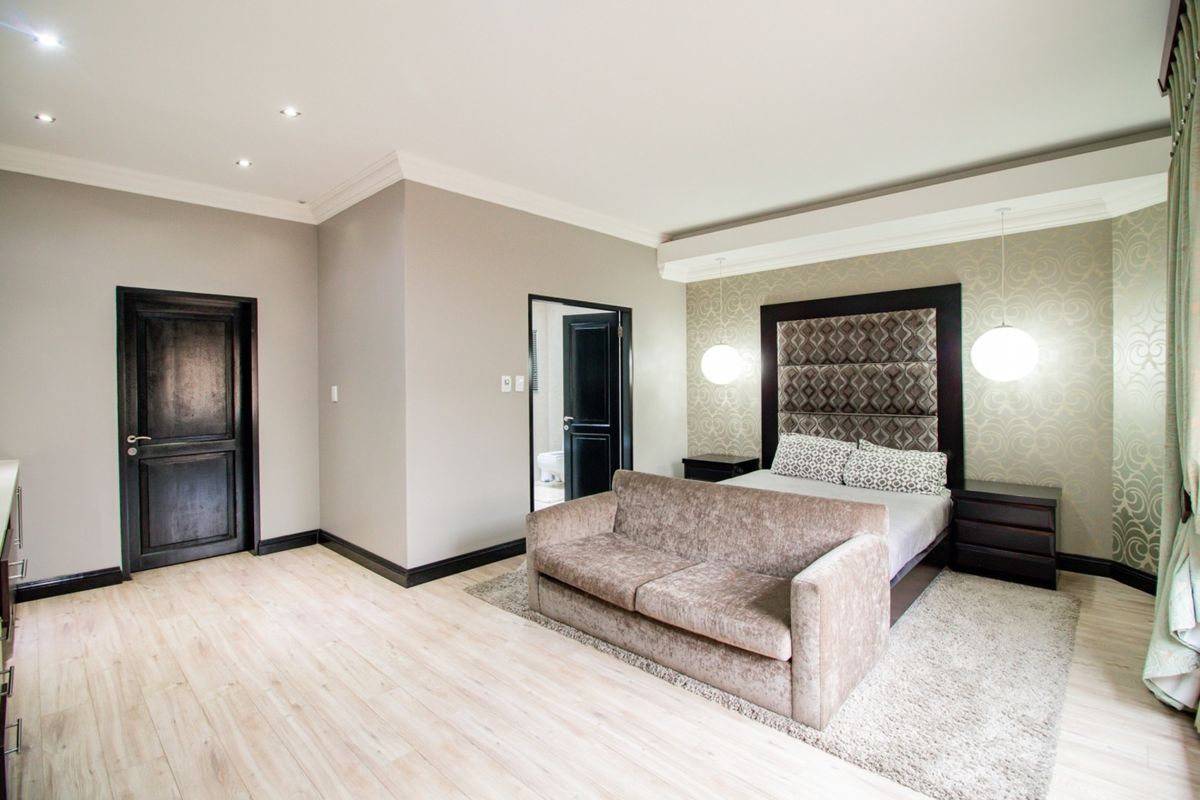 A spacious bedroom featuring modern laminate flooring, recessed downlighting, and a custom built-in headboard with integrated pendant lighting.