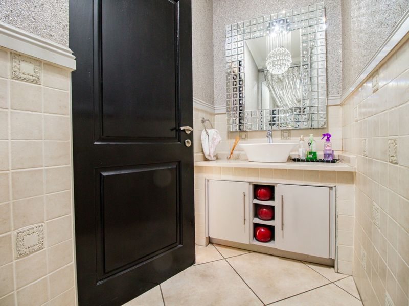 A compact bathroom featuring a vessel sink, vanity cabinet, tiled walls, and a decorative mirror.