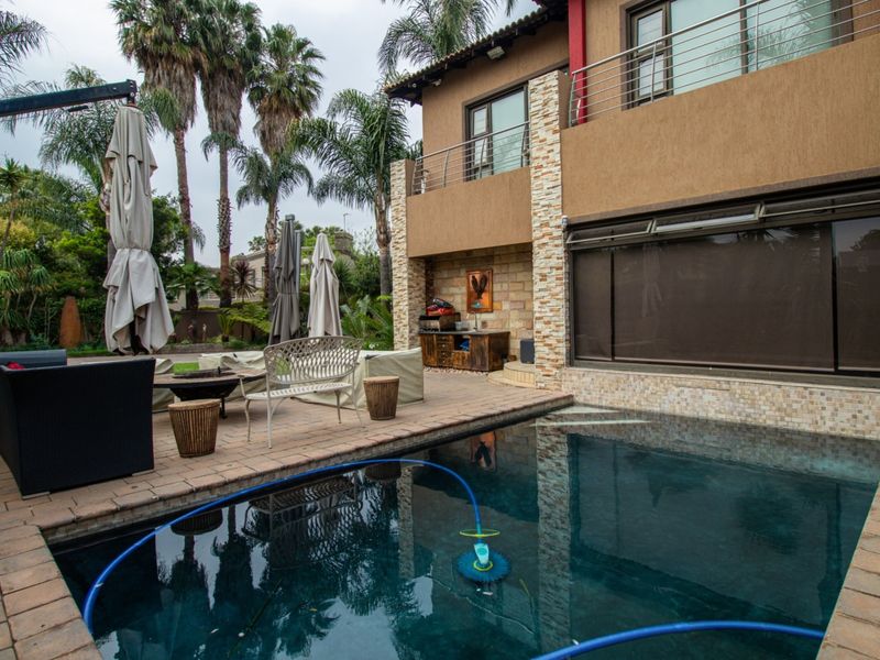 Outdoor entertainment area featuring a swimming pool, paved patio, and stone-clad exterior wall with a balcony above.