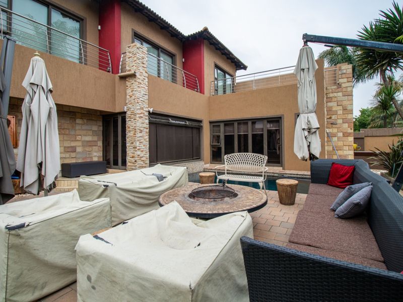 Spacious rear patio area featuring a swimming pool, stone-clad architectural details, and access to an upper-level balcony with stainless steel railings.