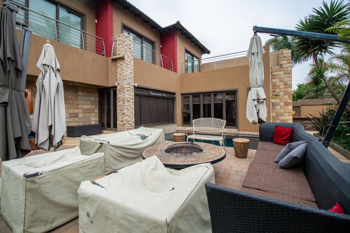 Spacious rear patio area featuring a swimming pool, stone-clad architectural details, and access to an upper-level balcony with stainless steel railings.