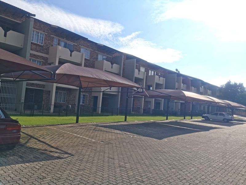 Exterior view of an apartment complex featuring a paved parking area with shade cloth carports and brick facade building design.