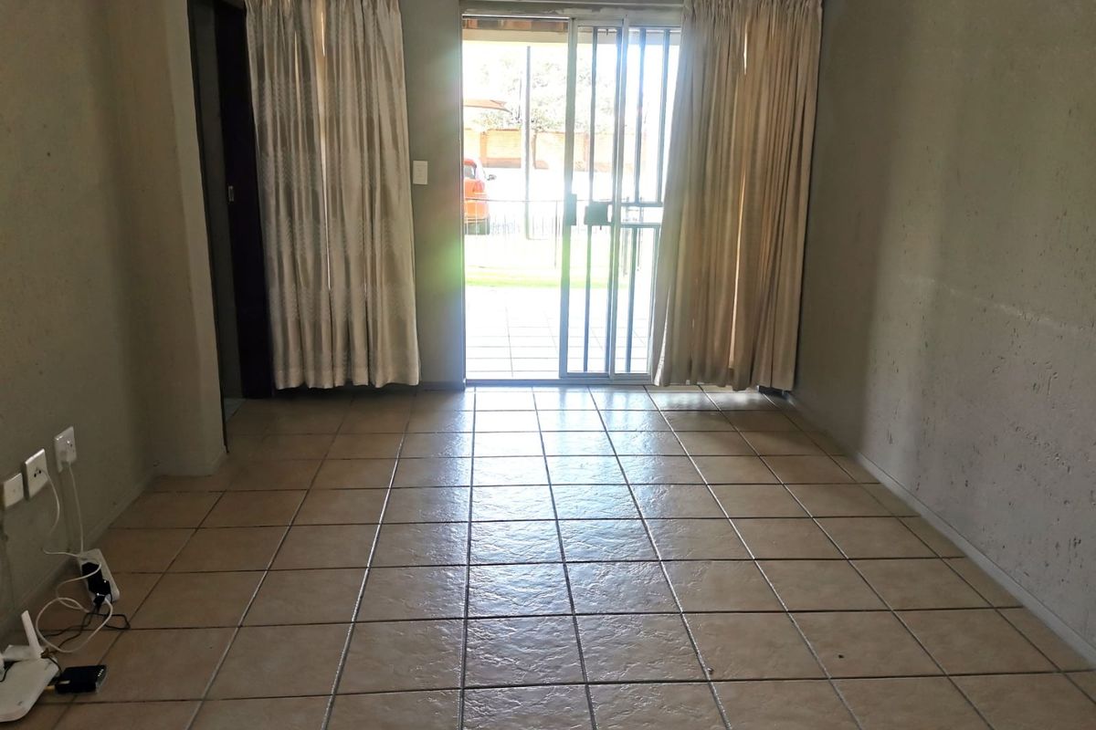 An empty living room featuring ceramic floor tiles and a sliding glass door with security gate leading to an outdoor area.