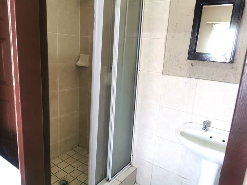 A functional bathroom featuring a shower enclosure with tiled walls and a pedestal basin, requiring some cosmetic updates to improve its overall condition.