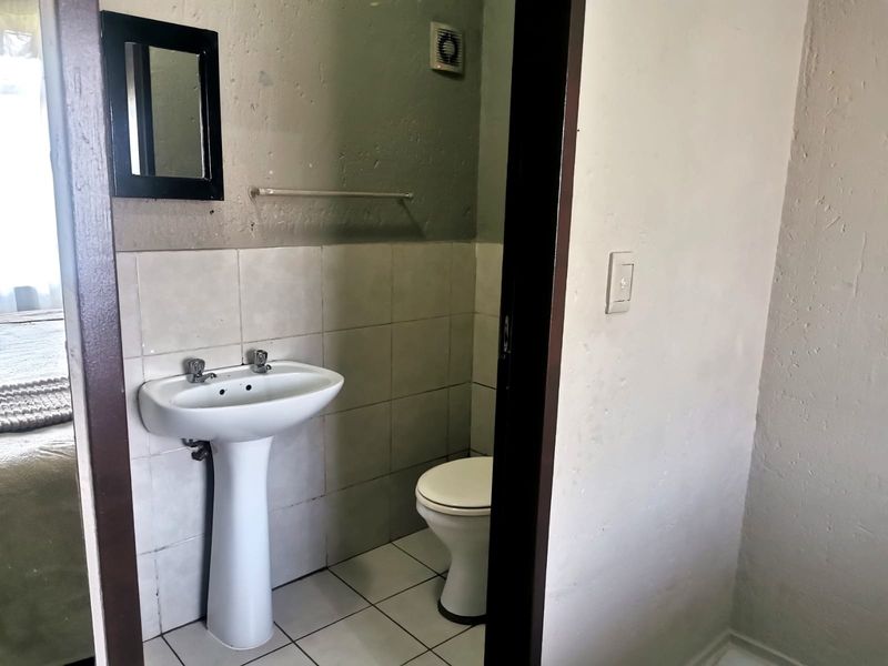 A compact bathroom featuring a pedestal basin, toilet, and extractor fan, with tiled flooring and splashbacks. The space requires cosmetic updates.