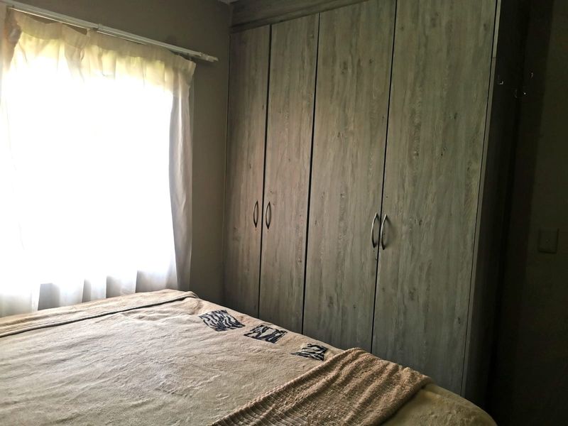 A bedroom featuring built-in wooden cupboards and a window with natural light.