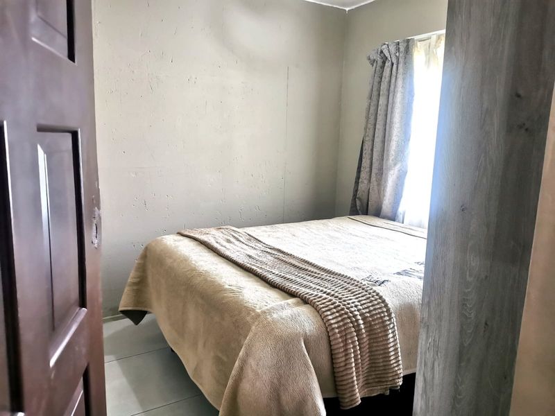 A compact bedroom featuring tiled flooring and a window, currently showing signs of wear on the wall surfaces.