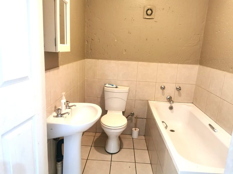 A functional bathroom featuring a pedestal basin, toilet, and bathtub with tiled flooring and wall splashbacks, requiring cosmetic updates to the wall finishes.