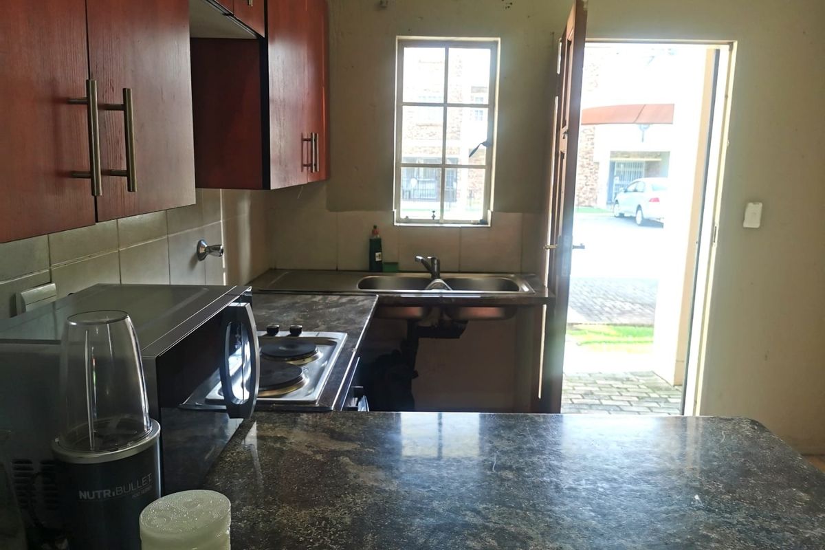 A compact kitchen featuring dark laminate countertops, built-in wooden cabinetry, an electric hob, and a stainless steel sink with direct access to the exterior.