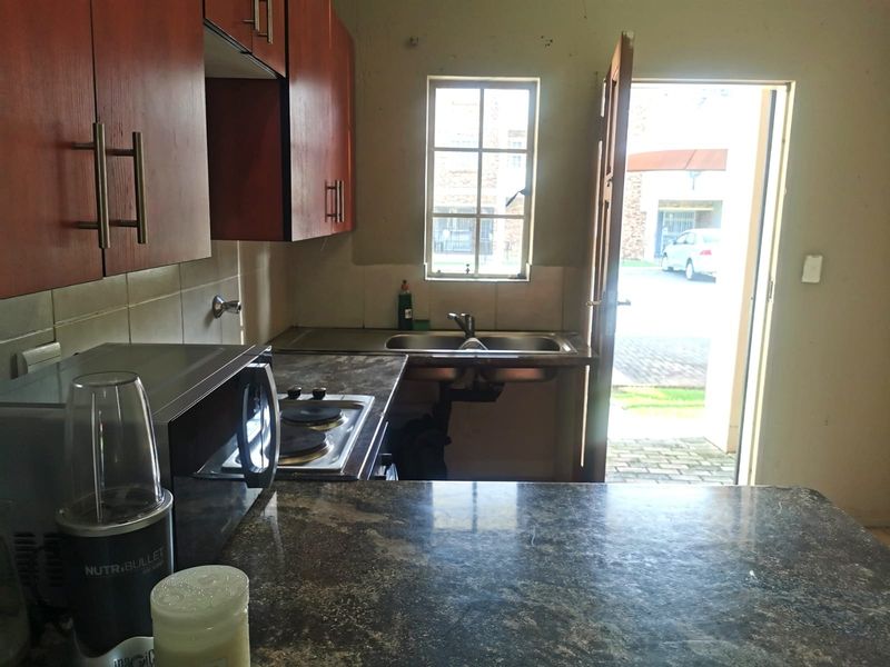 A compact kitchen featuring dark laminate countertops, built-in wooden cabinetry, an electric hob, and a stainless steel sink with direct access to the exterior.