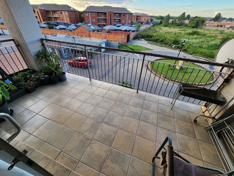 A spacious apartment balcony featuring tiled flooring and a metal balustrade, offering an elevated view of the surrounding complex and neighborhood.