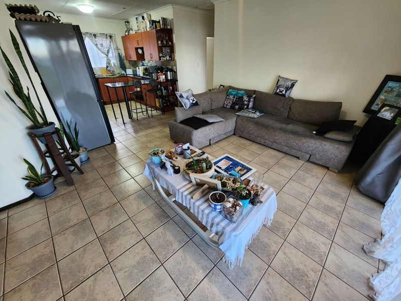 An open-plan living and kitchen area featuring tiled flooring, wooden cabinetry, and a breakfast bar, offering a functional layout for daily living.