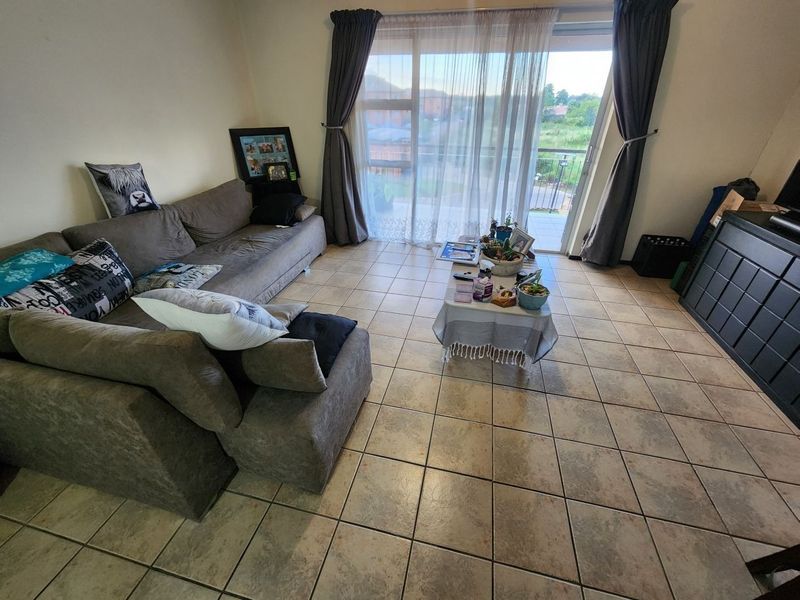 A living room featuring tiled flooring and a large sliding glass door that provides access to an outdoor balcony area.