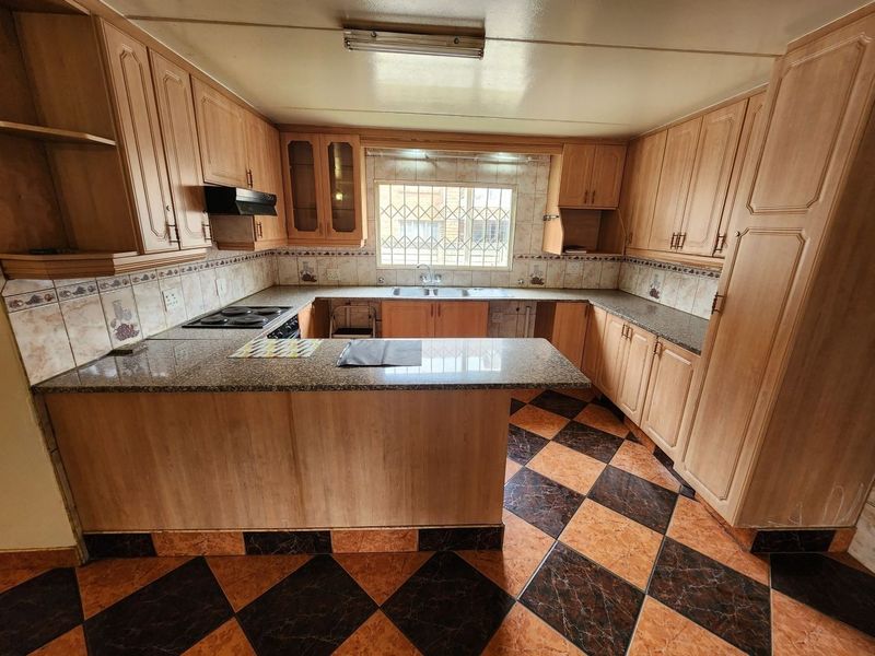 A functional kitchen featuring wooden cabinetry, granite countertops, a double basin sink, and a built-in electric hob with an extractor fan.