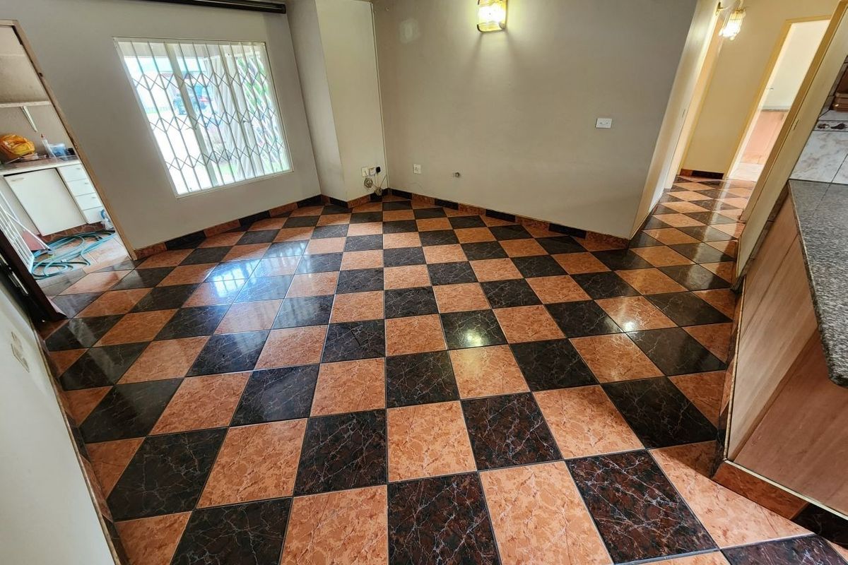 An empty living area featuring distinctive checkered ceramic floor tiles, a security-barred window, and direct access to adjacent rooms.