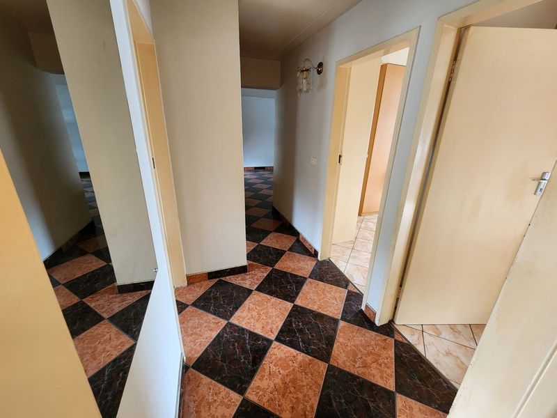 A functional hallway featuring a distinctive checkered tile floor, wall-mounted lighting, and access to multiple rooms within the apartment.