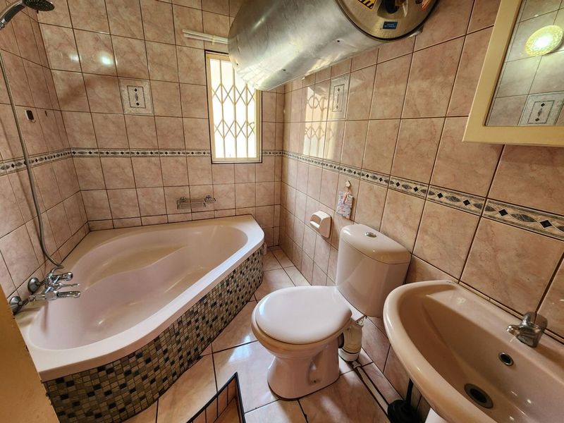 A functional bathroom featuring a corner bathtub, pedestal sink, toilet, and ceramic tiling, with an exposed water heater unit.