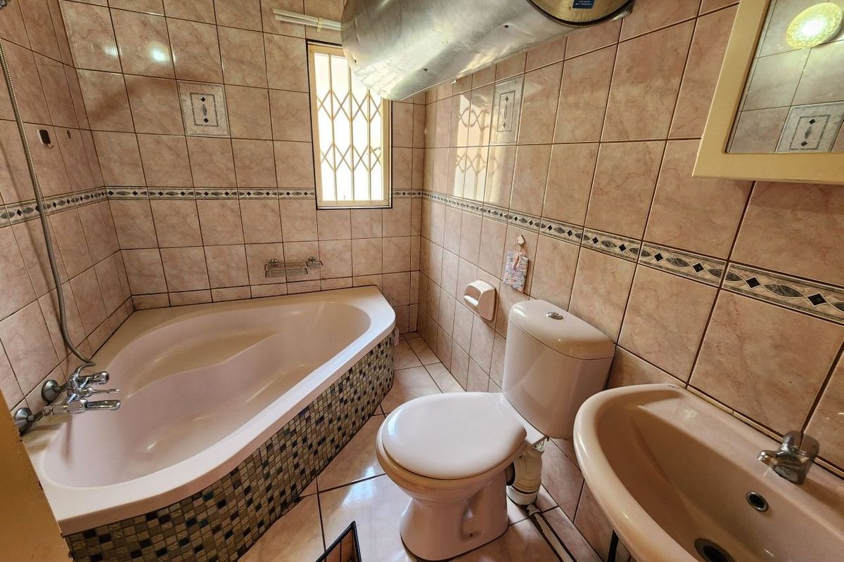 A functional bathroom featuring a corner bathtub, pedestal sink, toilet, and ceramic tiling, with an exposed water heater unit.