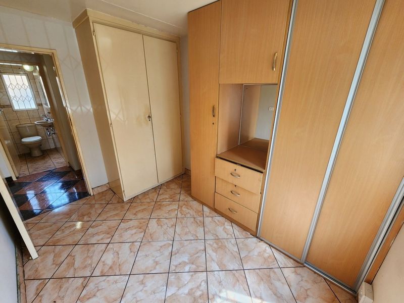 A bedroom featuring built-in cupboards and tiled flooring, with an adjacent view into a bathroom area.