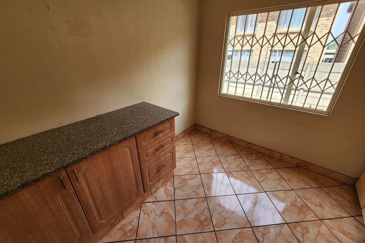 A compact kitchen area featuring built-in cabinetry with granite countertops, tiled flooring, and a window fitted with security bars.