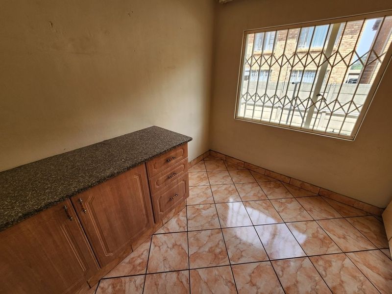 A compact kitchen area featuring built-in cabinetry with granite countertops, tiled flooring, and a window fitted with security bars.