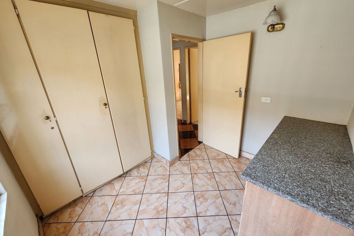 A functional bedroom featuring built-in cupboards, tiled flooring, and a granite-topped surface, offering a neutral canvas for potential updates.