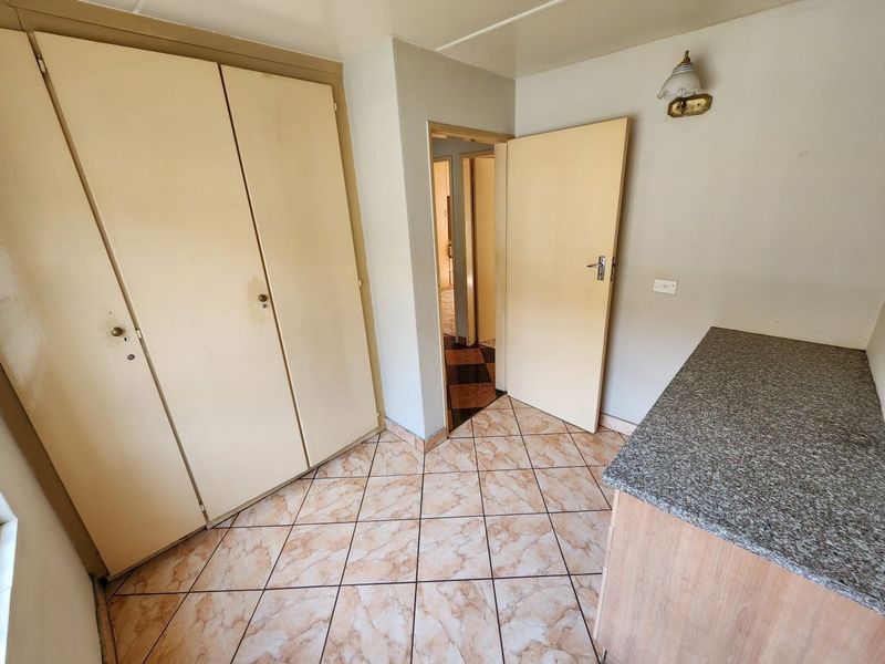 A functional bedroom featuring built-in cupboards, tiled flooring, and a granite-topped surface, offering a neutral canvas for potential updates.