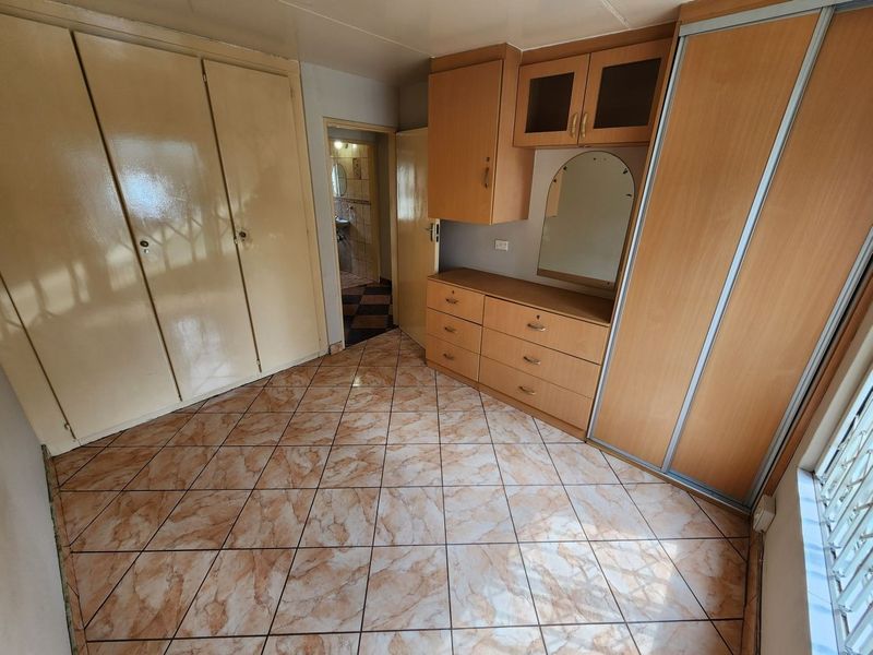 A bedroom featuring built-in cupboards, tiled flooring, and a vanity area, with an adjacent view into a bathroom.