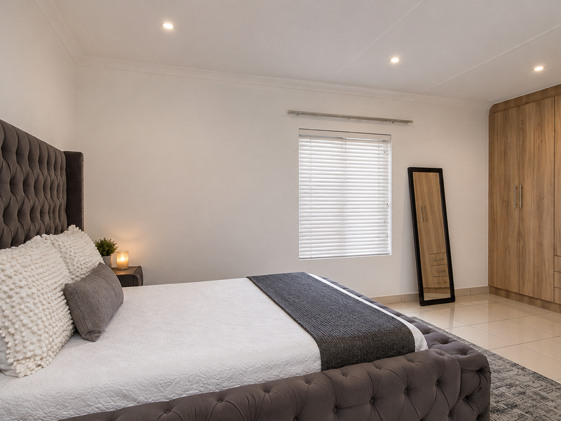 A well-maintained bedroom featuring modern built-in cupboards, neutral tiled flooring, and clean finishes with recessed lighting.