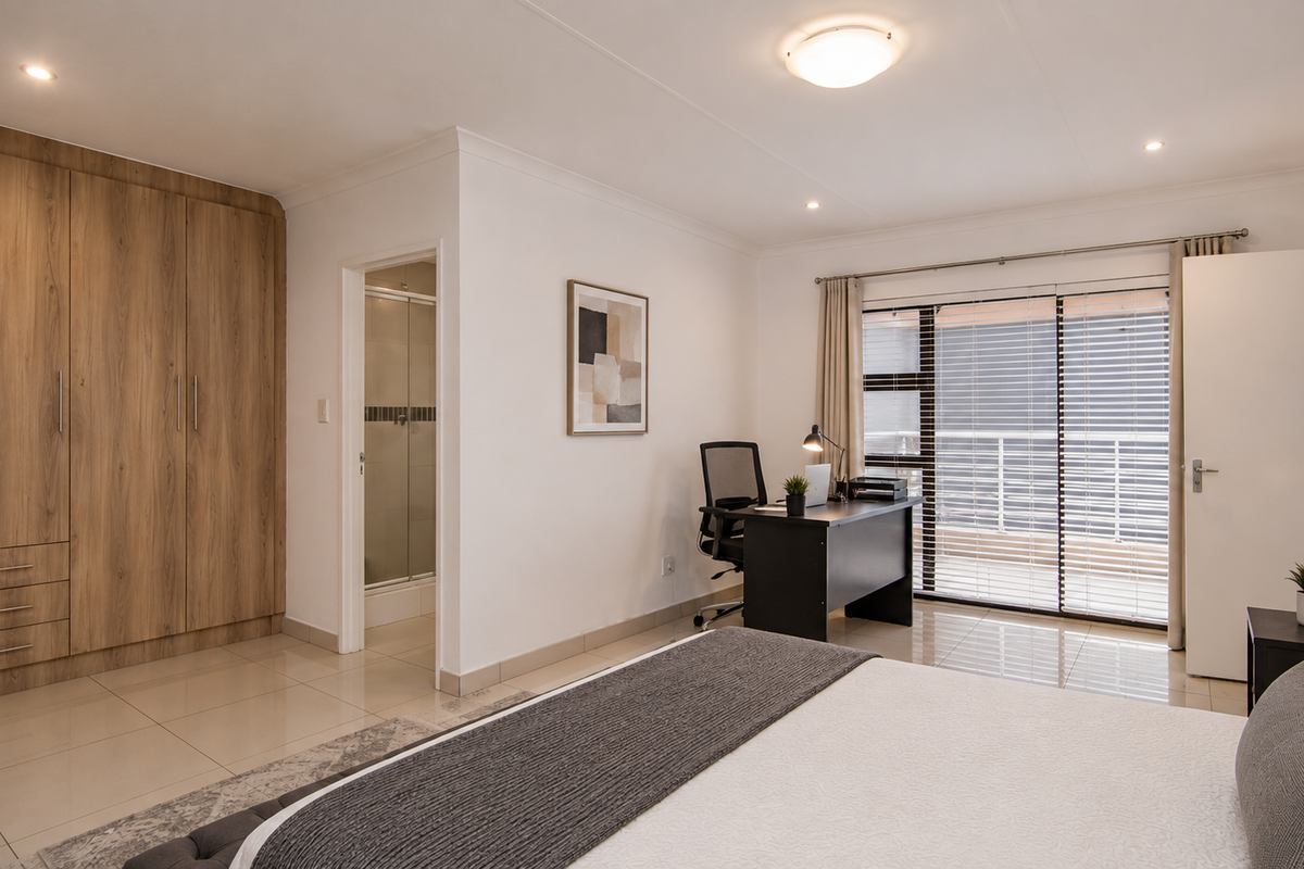 Spacious bedroom featuring built-in wooden cupboards, tiled flooring, and a sliding door leading to a balcony, with an adjoining en-suite bathroom.