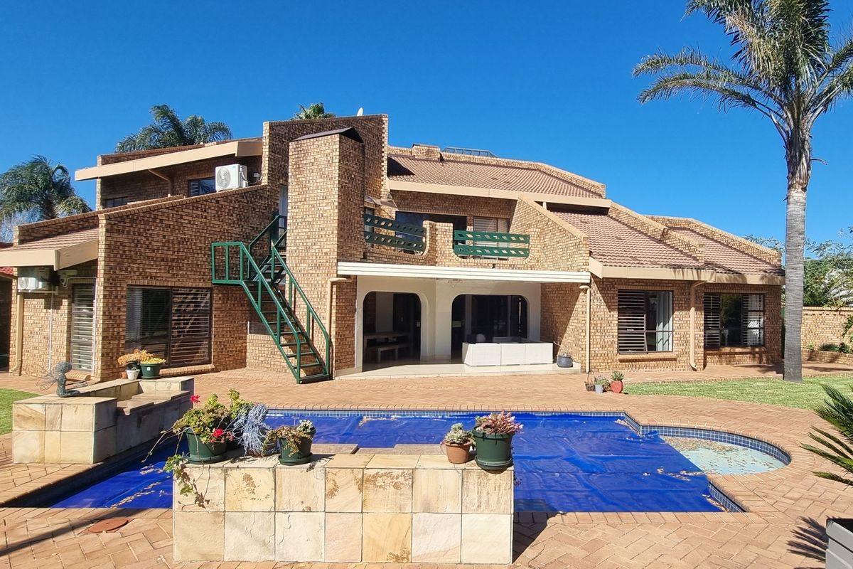 Rear view of a multi-level brick house featuring a swimming pool, covered patio, balcony, and an external staircase set within a landscaped garden.