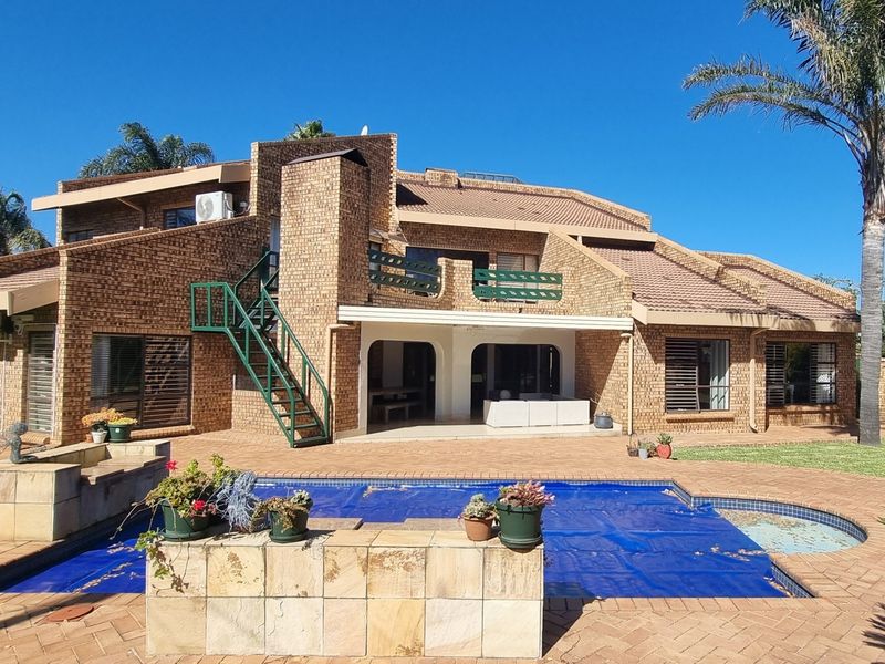 Rear view of a multi-level brick house featuring a swimming pool, covered patio, balcony, and an external staircase set within a landscaped garden.