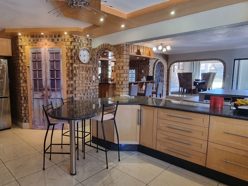 Spacious open-plan kitchen featuring granite countertops, light wood cabinetry, and distinctive brick archways, seamlessly connecting to the dining and living areas.