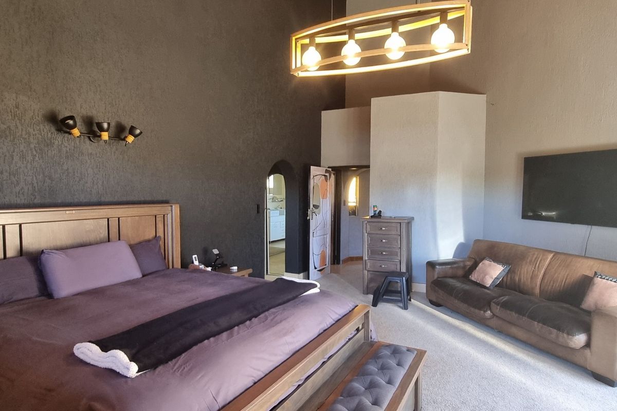 Spacious bedroom featuring a vaulted ceiling, textured dark accent wall, and an arched doorway leading to an adjoining space.