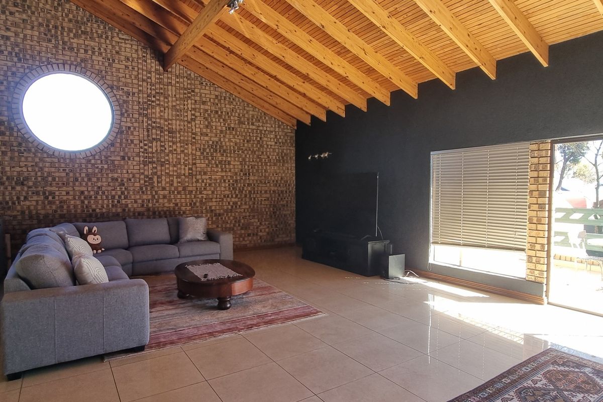 Spacious living room featuring a high exposed timber rafter ceiling, a striking brick feature wall with a circular window, and large sliding glass doors.