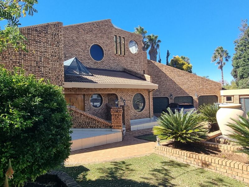 A distinctive face-brick front elevation featuring unique circular windows, a tiled roof, a skylight, and a well-maintained paved driveway with a double garage.