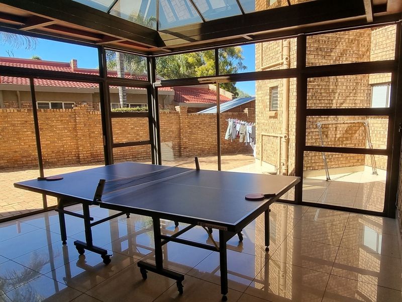 A bright, enclosed patio featuring a glass roof, tiled flooring, and large sliding glass doors that provide seamless access to the rear garden area.