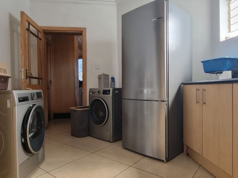 A functional laundry room featuring tiled flooring, built-in cabinetry with laminate countertops, and space for multiple appliances.