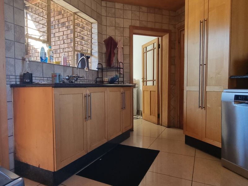 A functional kitchen featuring light wood cabinetry, granite countertops, tiled backsplash, and integrated dishwasher, offering a practical layout with direct access to adjacent rooms.