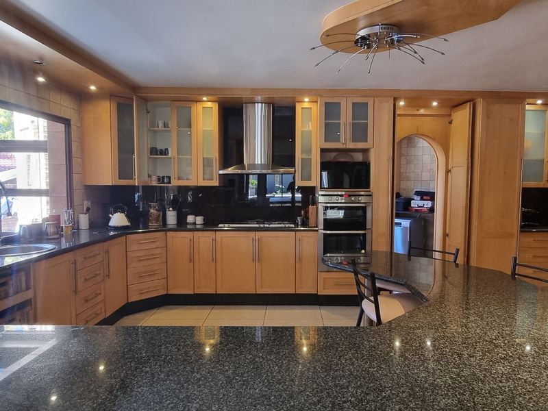 Spacious kitchen featuring extensive wooden cabinetry, granite countertops, built-in appliances, and a large breakfast bar island with recessed lighting.